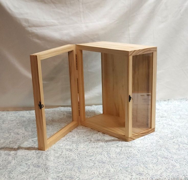 an open wooden box sitting on top of a white tablecloth covered floor next to a wall