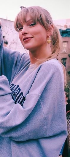 a woman with blonde hair wearing a blue sweatshirt and gold hoop earrings standing in front of a building