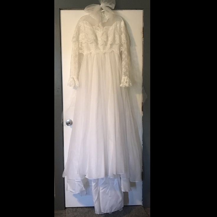 a white dress hanging on a door with a bow at the neck and long sleeves