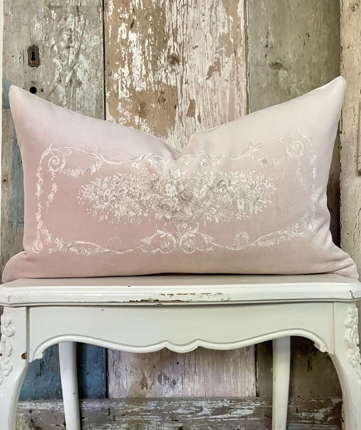 a pink pillow sitting on top of a white bench next to a wooden wall with peeling paint