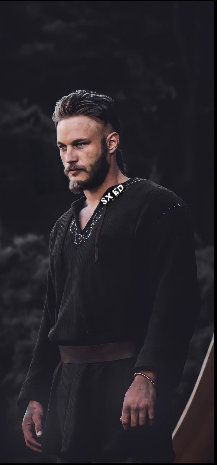 a man with long hair and beard standing in front of a dark background wearing a black sweater