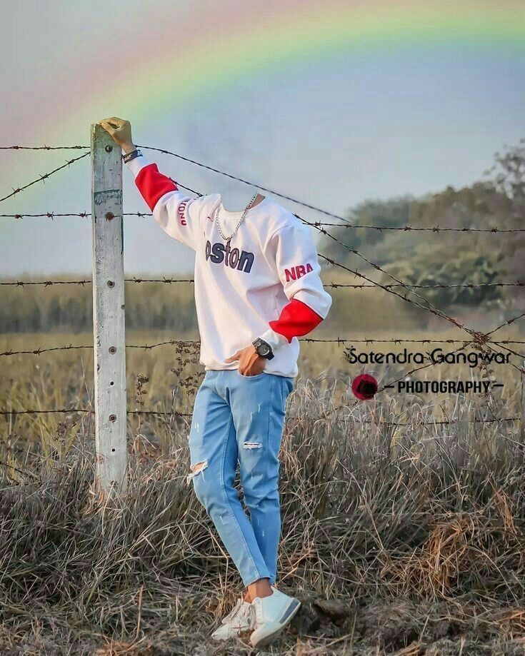 a man standing next to a barbed wire fence with a rainbow in the sky behind him