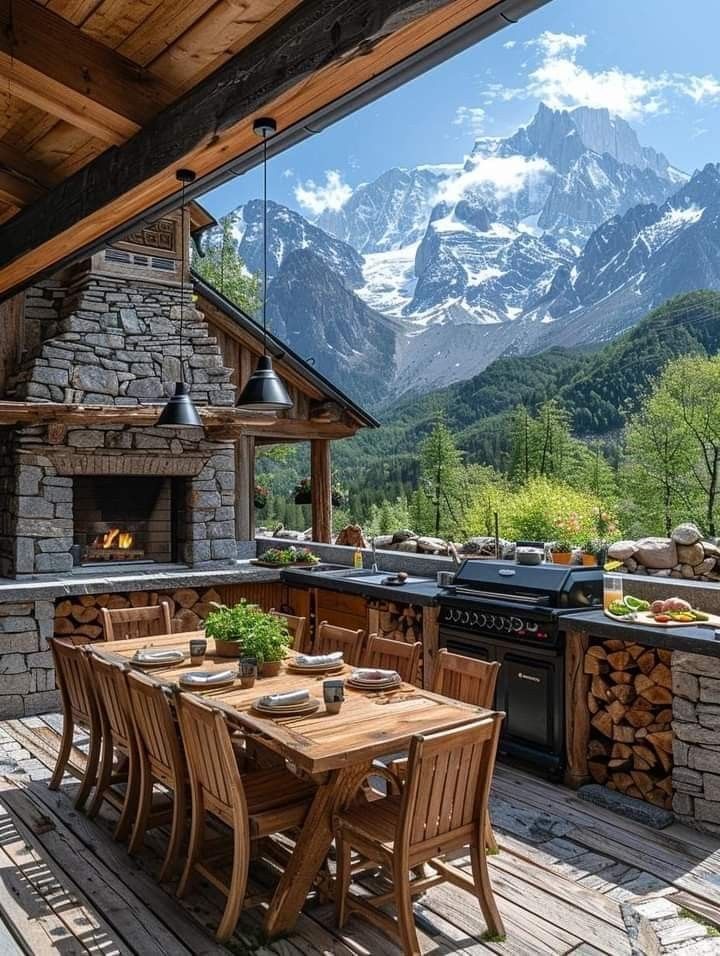 an outdoor kitchen and dining area with mountains in the background, surrounded by wood flooring