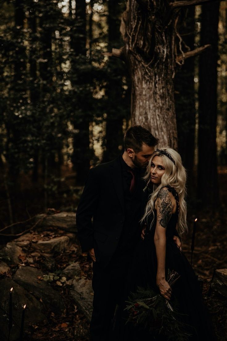 a man and woman standing next to each other in the woods