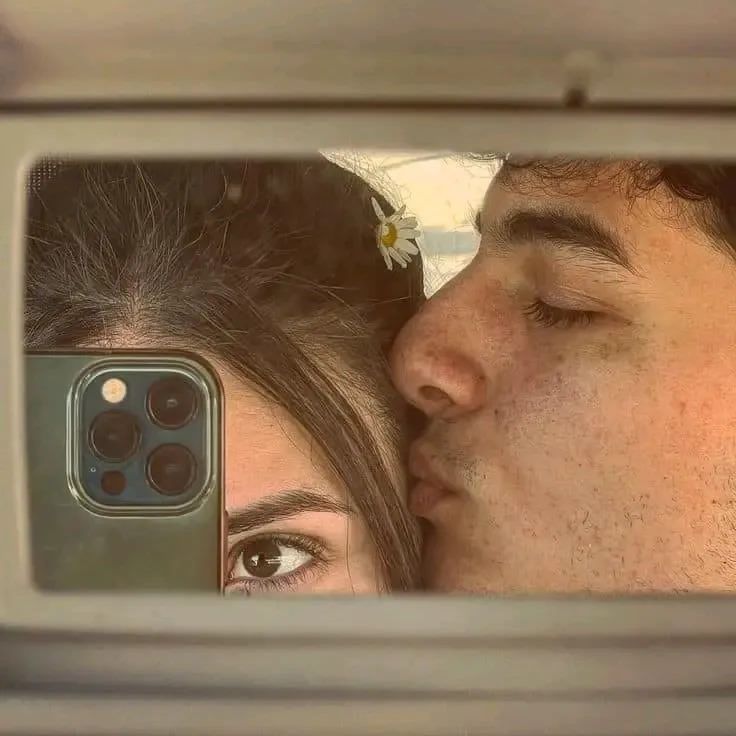 a man and woman kissing in front of a mirror with the reflection of their cell phone