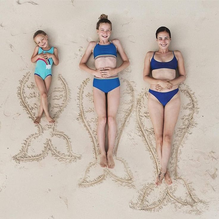 three women in bikinis laying on the sand with their arms around each other and smiling