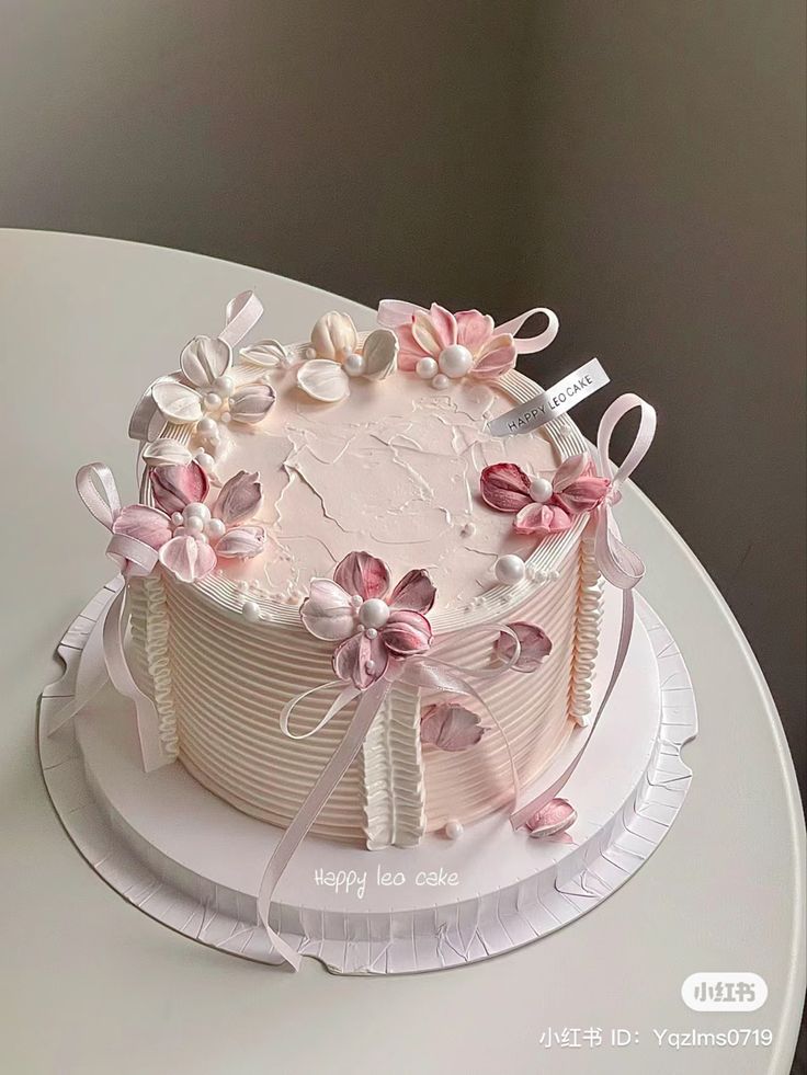 a white cake with pink flowers and ribbons