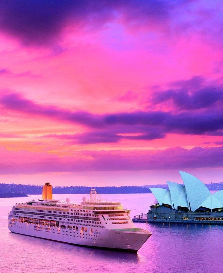 a large cruise ship in the water near a blue and pink building with an opera on it's side