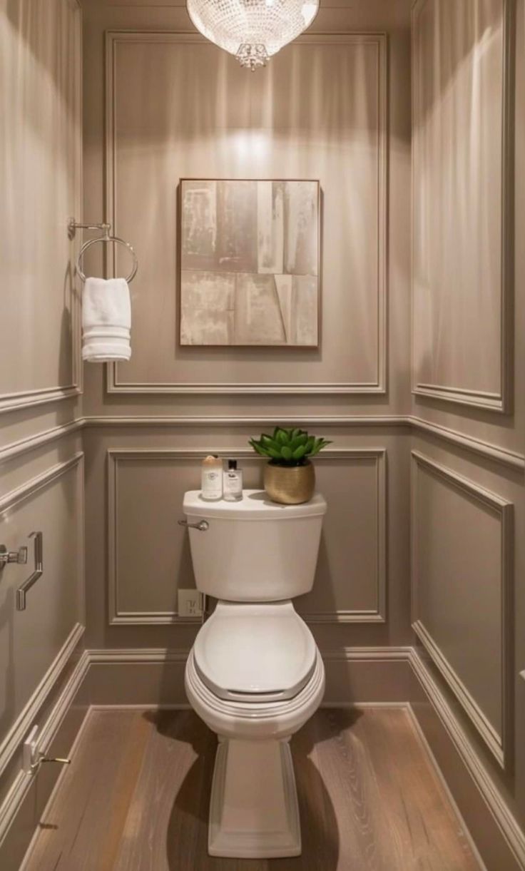 a white toilet sitting inside of a bathroom next to a wooden floor and light fixture