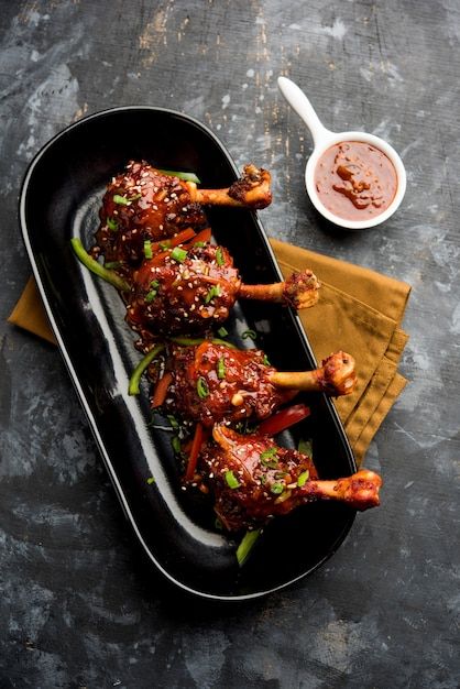 two chicken legs covered in sauce and garnished with scallions on a black platter