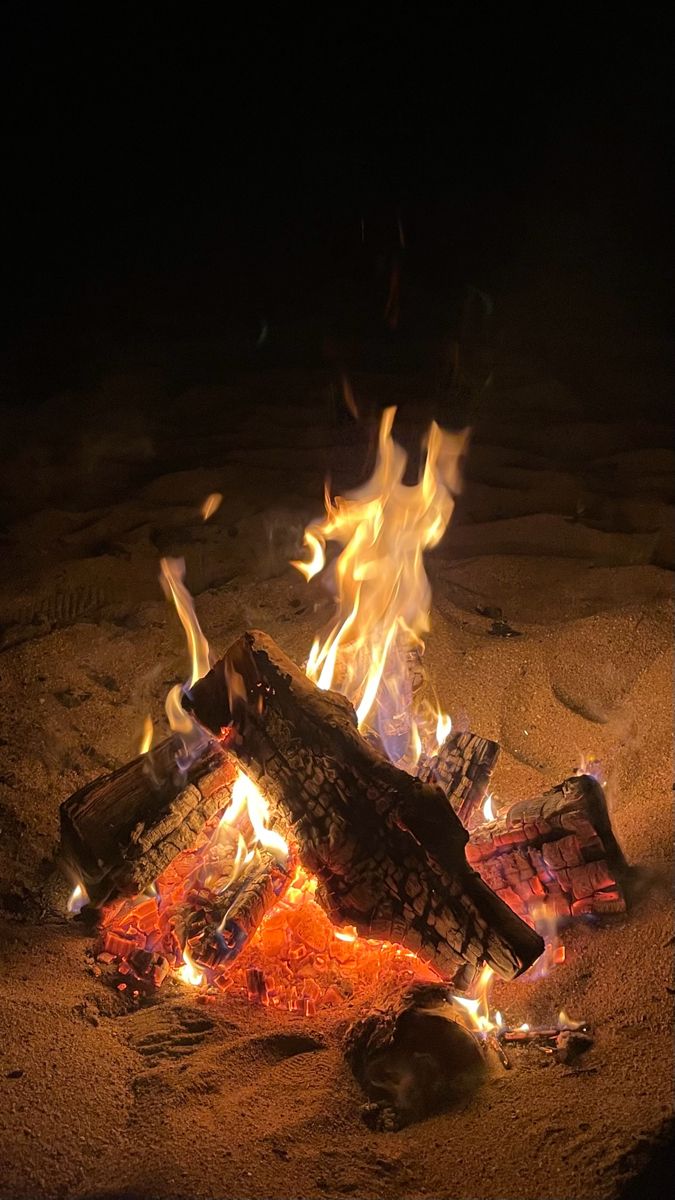 the fire is burning in the dark on the sand and there are no people around it