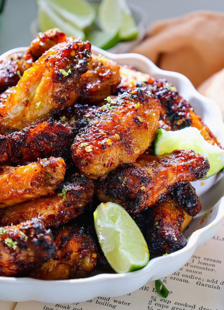 a white bowl filled with chicken wings and lime wedges