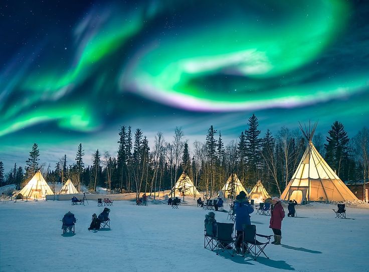 people are sitting in the snow near tents under an aurora borel sky with green and purple lights