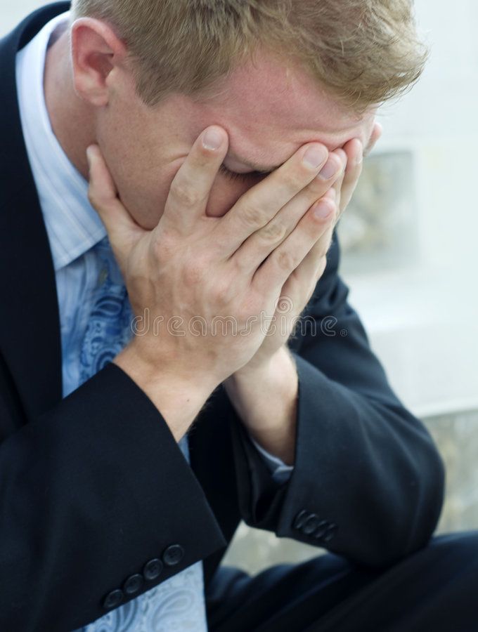 a man in a suit holding his hands to his face while sitting on the floor