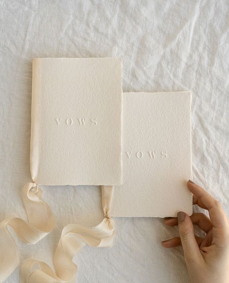 two white cards with the words vows written on them are being held by someone's hand