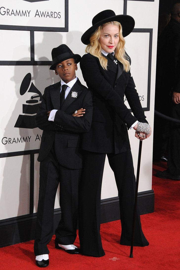 two people in black suits and hats standing on a red carpet with their arms around each other