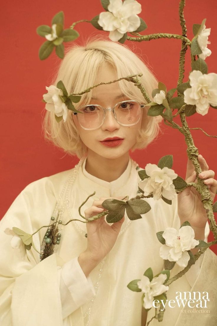 a woman wearing glasses and holding flowers in front of her face while standing next to a branch