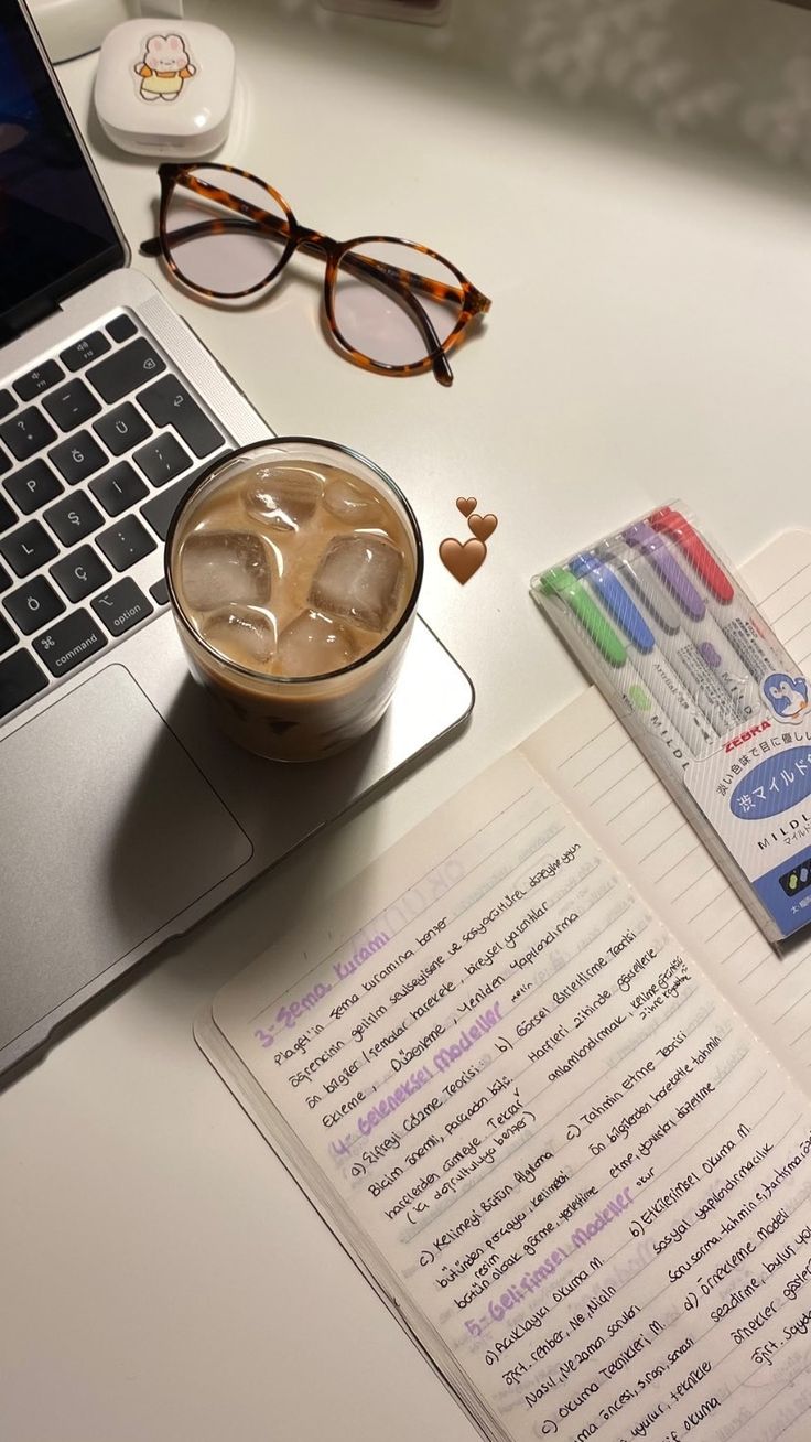 a cup of coffee and notebook on a desk with eyeglasses next to it