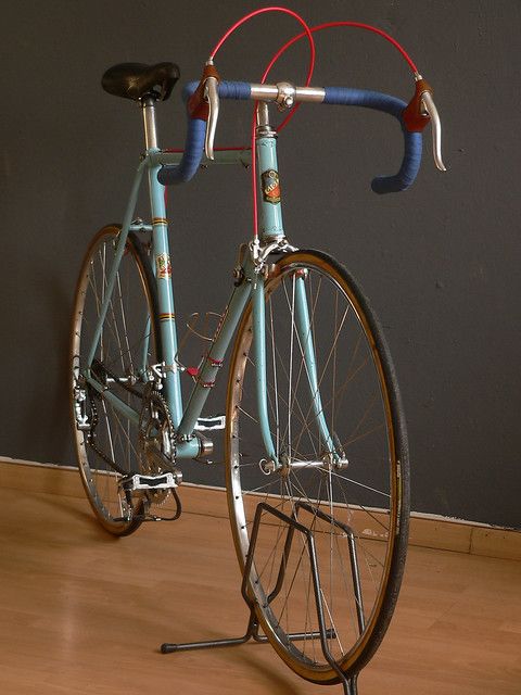 a blue bicycle parked on top of a hard wood floor next to a gray wall