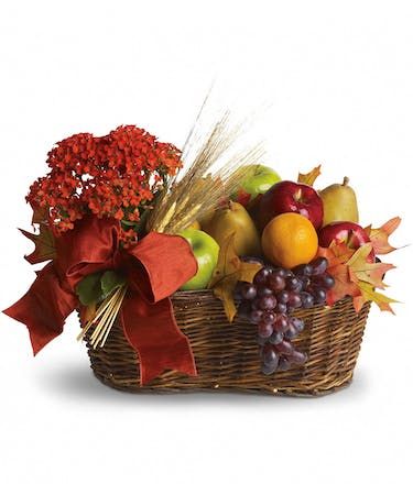 a basket filled with fruit and flowers on top of a white background, next to a red bow