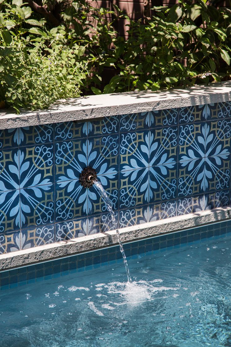 a blue and white tiled wall next to a pool with water coming out of it