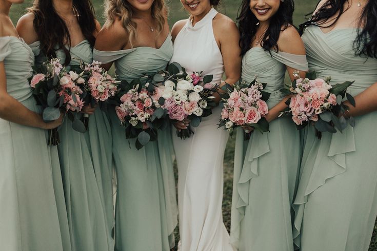 a group of women standing next to each other wearing dresses and holding bouquets in their hands