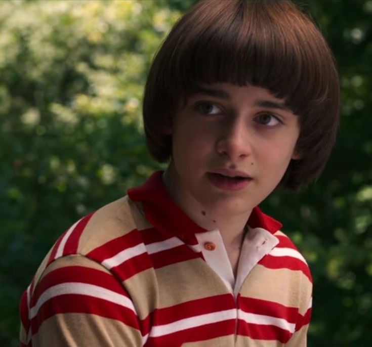 a young boy with brown hair wearing a red and white striped shirt looking at the camera