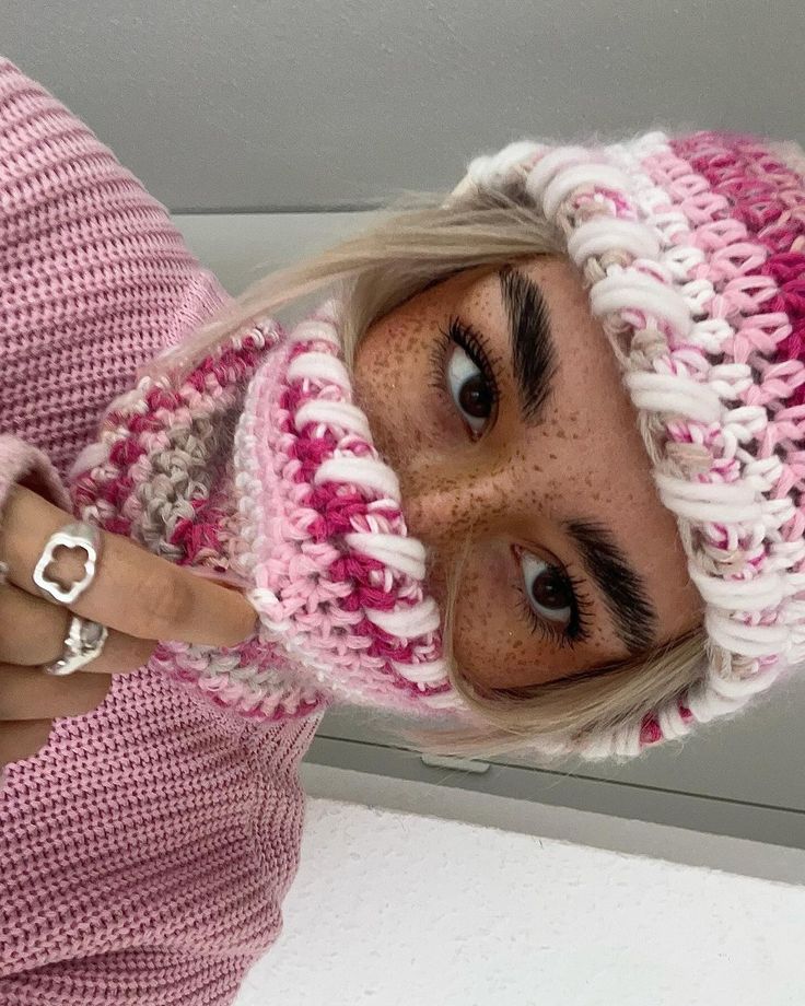 a woman with blonde hair wearing a pink and white knitted hat looking at the camera