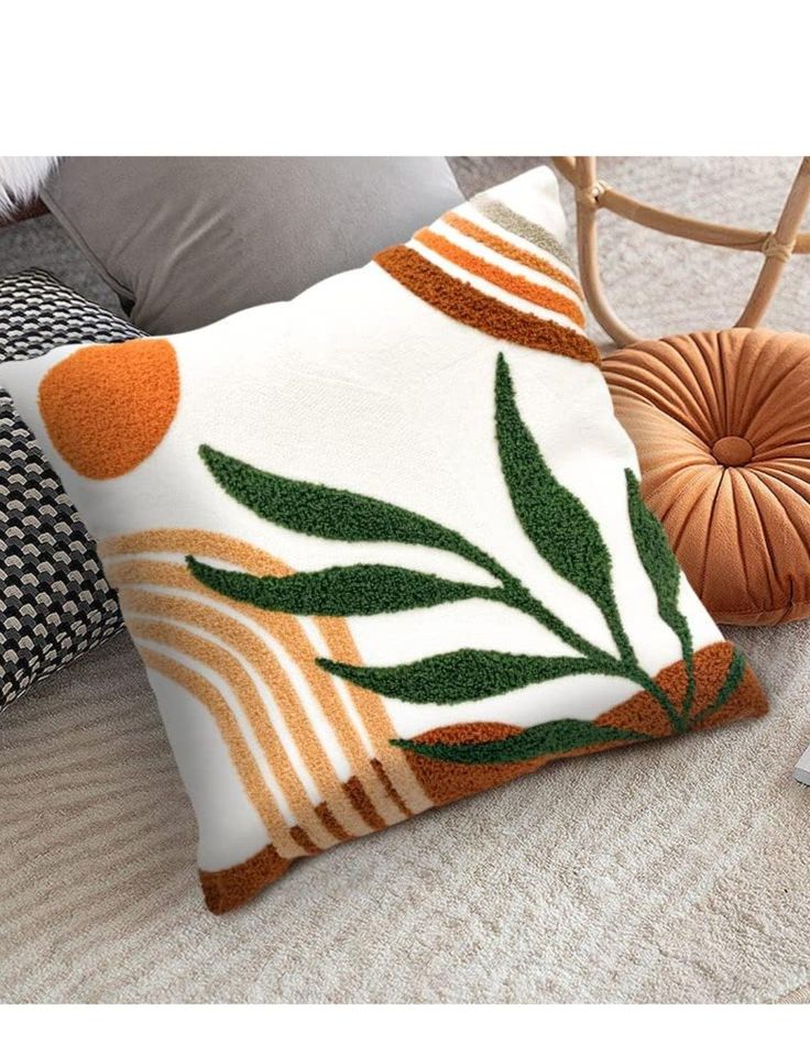 a white pillow with orange and green leaves on it sitting next to a brown chair