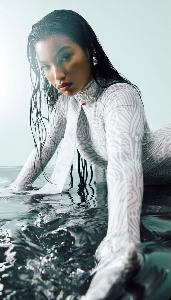 a woman in the water with her hands on her hips and wearing white clothing, posing for a photo