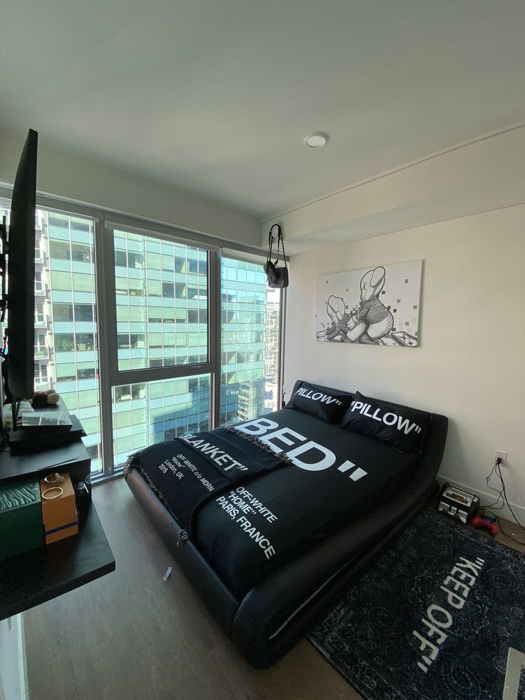 a bed sitting in the middle of a living room next to a window with large windows