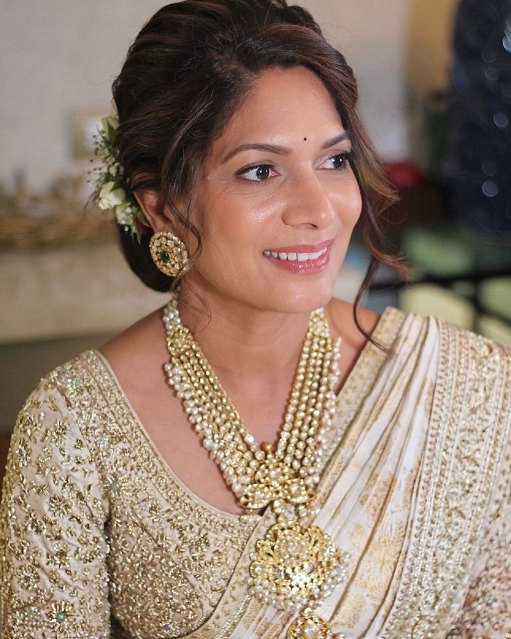 a woman wearing a gold and white sari with pearls on her neck, smiling at the camera