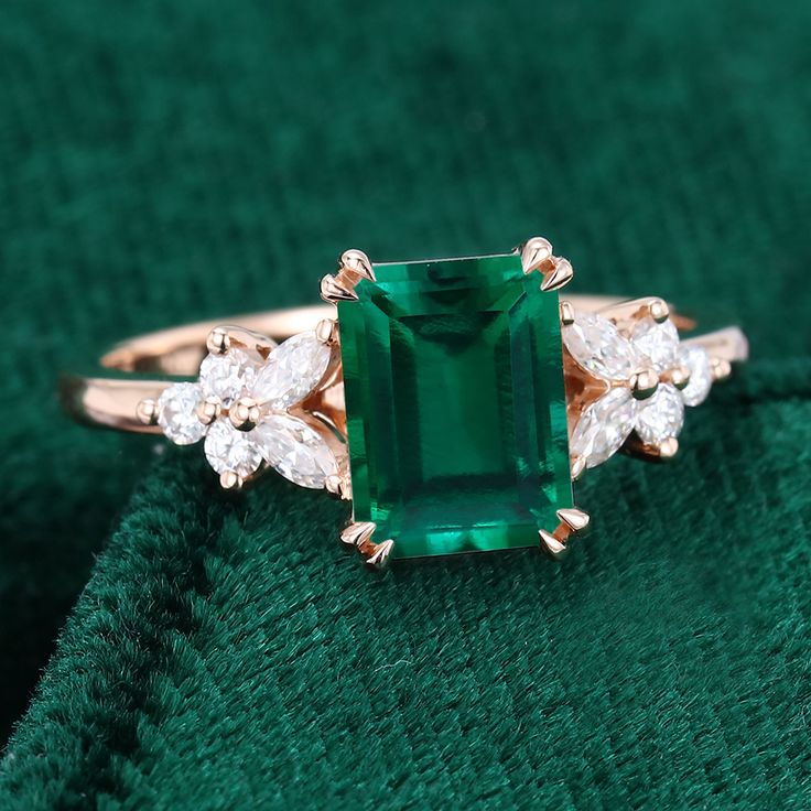 an emerald and diamond ring sitting on top of a green velvet cloth with three diamonds around it