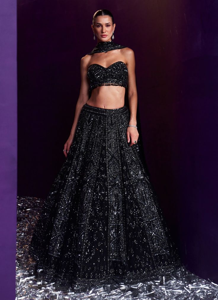 Elevate your style with the exquisite Black Sequins Embroidered Bridal Lehenga Set, a true masterpiece of craftsmanship and design. Crafted from soft net, the black lehenga is beautifully adorned with intricate embroidery featuring tonal and gunmetal sequins, glass pipes, and shimmering crystals, creating a mesmerizing interplay of light and texture. Teamed with a stylish tube-cut blouse, this set adds a contemporary twist to the traditional silhouette, offering a flattering and modern fit. The ensemble is completed with a matching embellished dupatta that exudes sophistication, making it a perfect choice for brides or brides-to-be looking to make a statement at cocktail parties, ensuring you stand out with grace and style on your special day. Composition : Lehenga, Blouse and Dupatta - Ne Tube Blouse Lehenga, Black Colour Lehenga, Black Choli With Resham Embroidery For Navratri, Cocktail Lehenga, Traditional Black Sets With Sequins, Black Bridal Lehenga, Black Sets With Intricate Embroidery For Receptions, Black Fitted Sharara For Evening, Black Anarkali Set For Evening Festivals