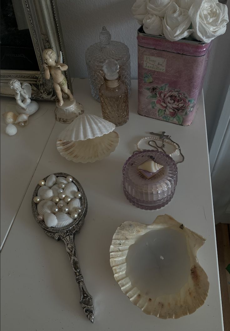 there are many shells on the table next to a mirror and a vase with flowers in it