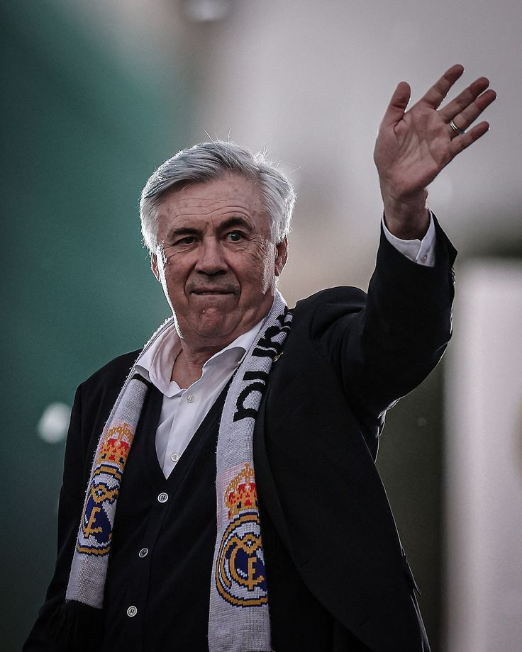 an older man waves to the crowd while holding his hand up in the air and wearing a scarf around his neck