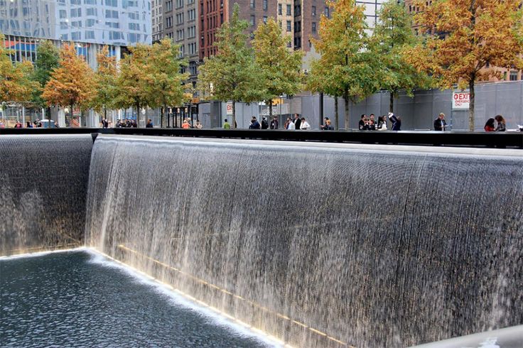 people are standing at the base of a large waterfall with water running down it's sides