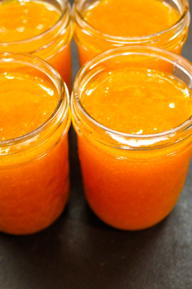 four jars filled with orange liquid sitting on top of a black table next to each other