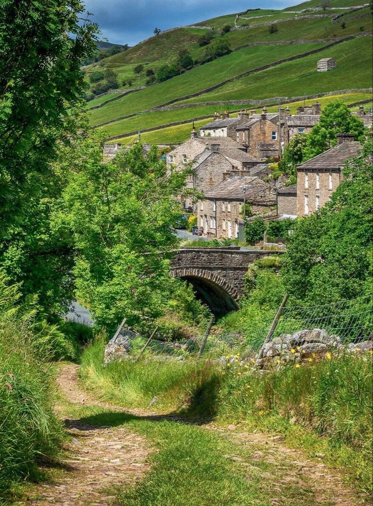 an old stone bridge over a small stream in the middle of a lush green hillside