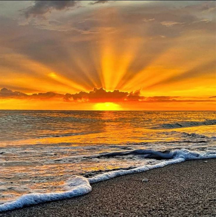 the sun is setting over the ocean with waves coming in to shore and clouds above