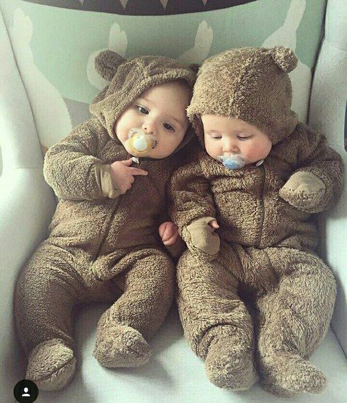 two babies dressed in bear costumes sitting on a chair with pacifier in their mouth