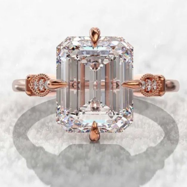 an emerald - cut diamond ring with two diamonds on the band and side stones in rose gold