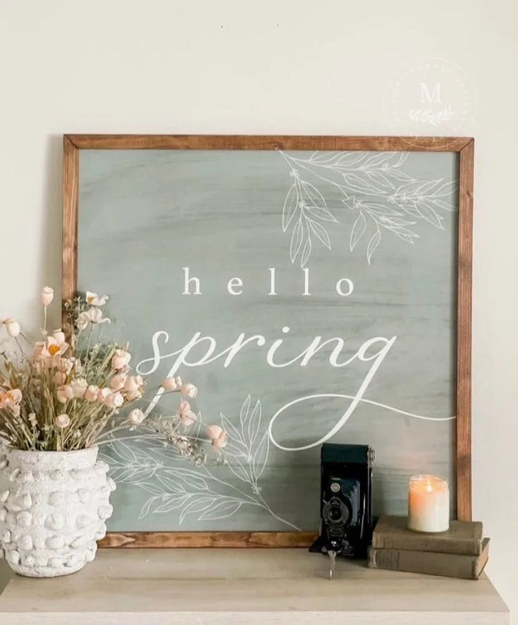 a sign that says hello spring next to a vase with flowers and books on it