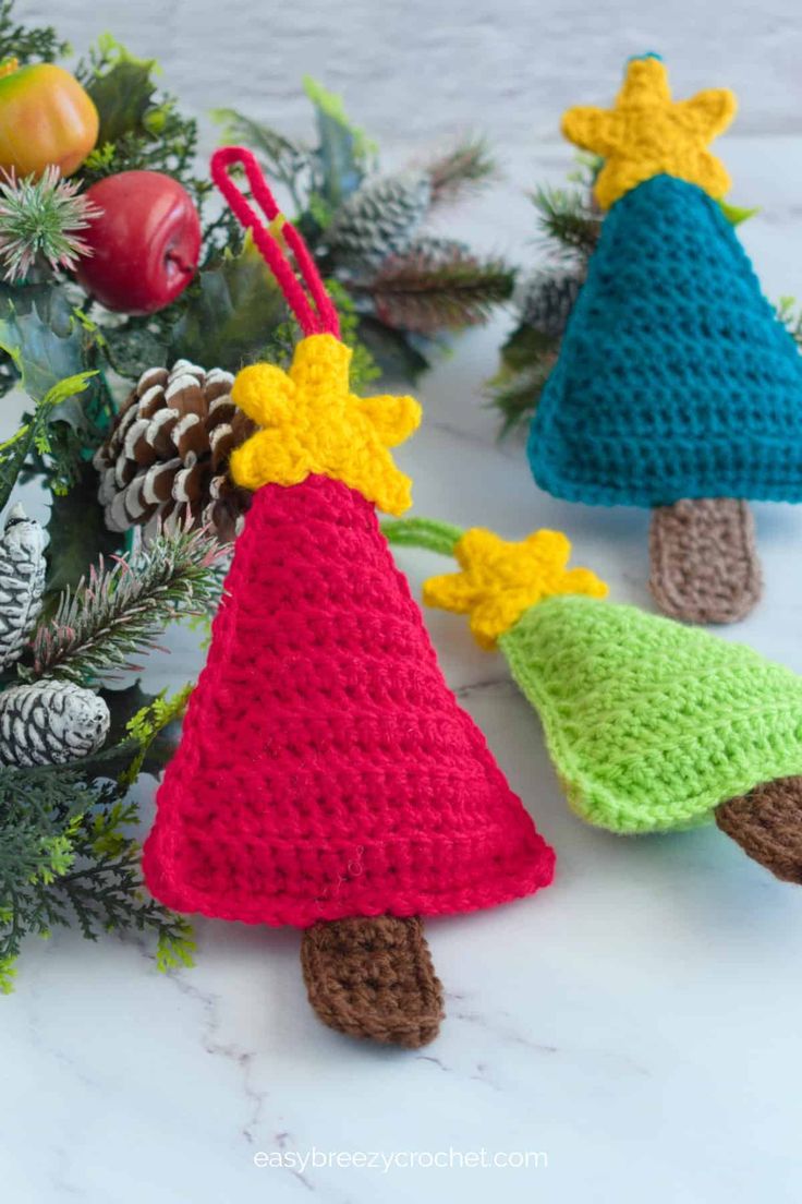 crocheted christmas tree ornaments with pine cones and bells on them, sitting next to evergreen branches