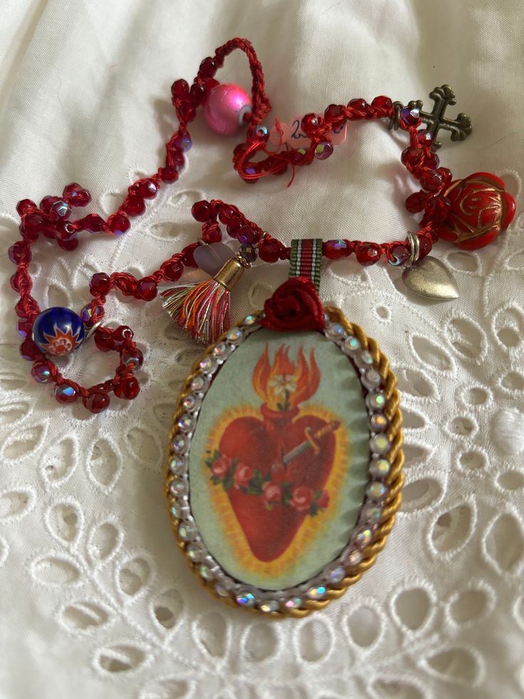 Textile necklaces  featuring the symbol of immaculate heart of Mary, or other saints  and angels.  Suspended on a crocheted cord, red cut beads with a lustrous effect.  The cord is further embellished with pendants made from historical pressed beads in the shape of roses as well as other shapes, like hearts and a brass cross.  The cord is finished with a loop and a large bead for closure.  The length of the crocheted  cord is 50 cm. Handmade Red Jewelry For Souvenir, Spiritual Red Necklace With Heart Charm, Crocheted Cord, The Immaculate Heart Of Mary, Immaculate Heart Of Mary, Heart Of Mary, Textile Necklace, Immaculate Heart, Pinterest Diy Crafts