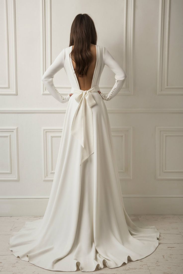 the back of a woman's wedding dress with long sleeves and a bow at the waist