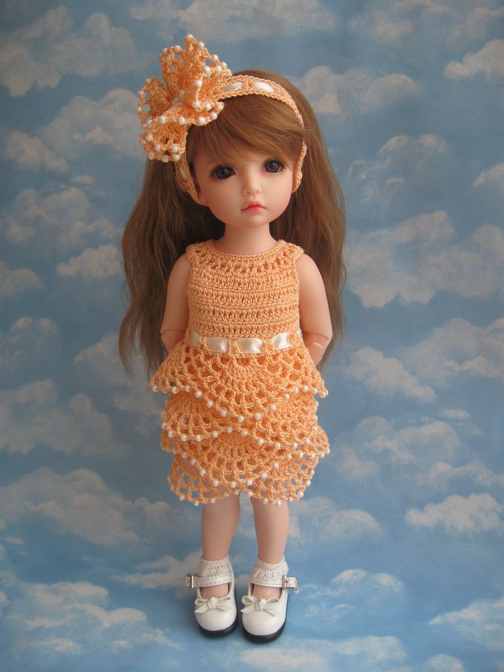 the doll is wearing a crocheted dress and shoes with pearls on her head