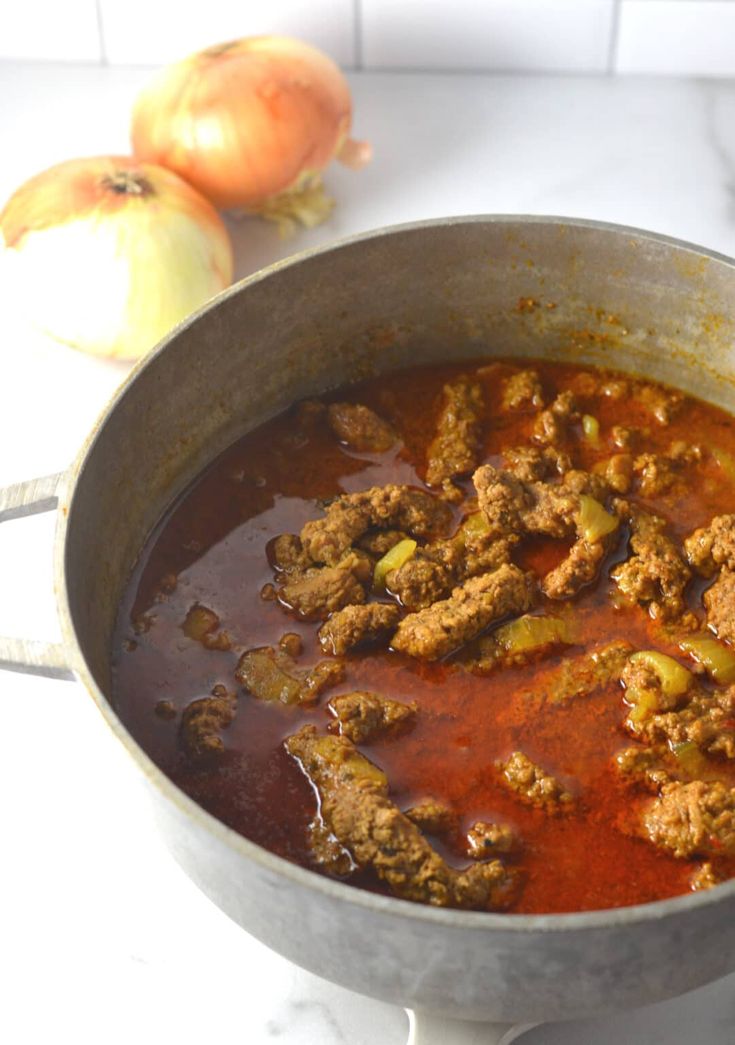 a pot filled with meat and vegetables on top of a counter next to an onion