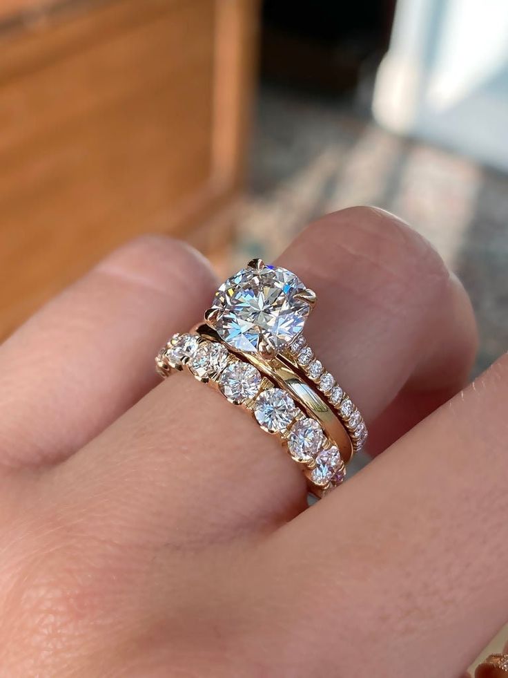 a woman's hand with a gold ring and two diamond wedding bands on it