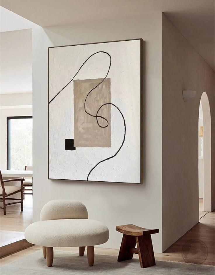 an abstract painting hangs on the wall next to a white chair and footstool